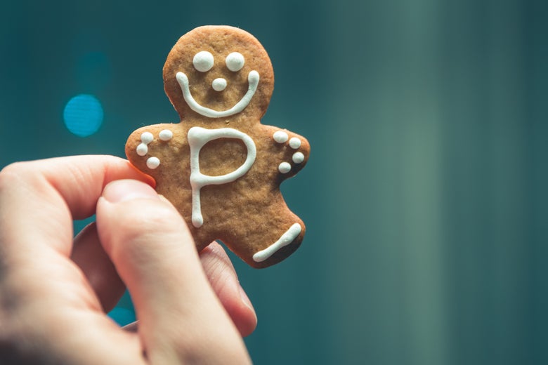 A hand holds up a gingerbread human-shaped cookie with the letter P on its torso.